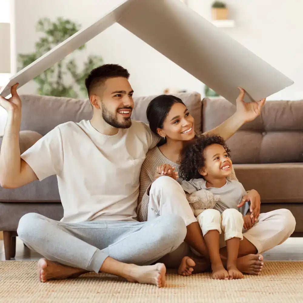 Ein beige Pappkartonhaus-förmige Spielkonstruktion, die von einer Familie hochgehalten wird.